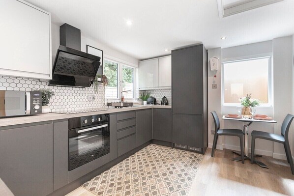 A modern kitchen with a microwave, oven, and dark cabinetry. There is a dining area with a table and chairs.