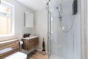 A modern bathroom with a glass-enclosed shower, a wooden vanity, a white sink, and a mirror above the vanity.