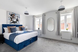 A modern bedroom with a large bed, a round mirror, and a painting on the wall.