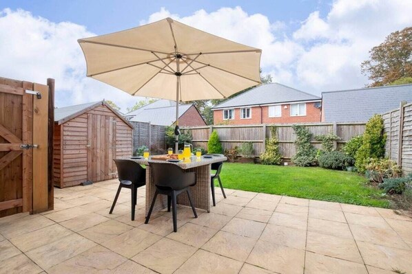 An outdoor patio with a table and chairs, a large umbrella, and a wooden fence in the background.