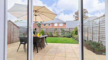 A patio with a table and chairs, a large umbrella, and a view of a residential area with houses and a wooden fence.