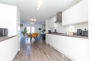 Una cocina moderna con armarios blancos, un comedor con sillas anaranjadas y una isla central.