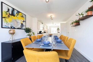 Un comedor con una mesa larga dispuesta para seis comensales, sillas amarillas y un cuadro abstracto moderno en la pared.