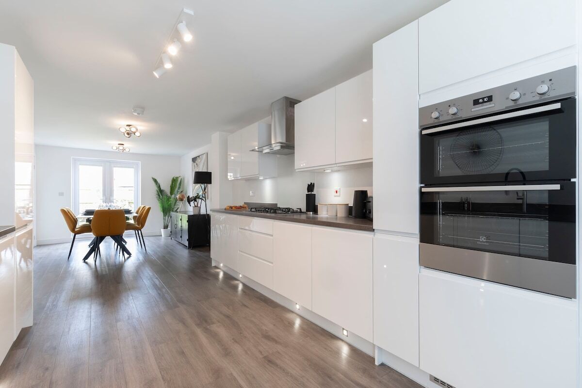 A modern kitchen with white cabinetry, a double oven, and a dining area with a yellow table and chairs.