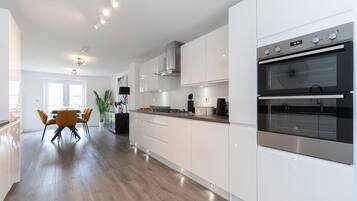 A modern kitchen with white cabinetry, a double oven, and a dining area with a yellow table and chairs.
