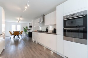 Une cuisine moderne avec des meubles blancs, un four double et un coin repas agrémenté d’une table et de chaises jaunes.