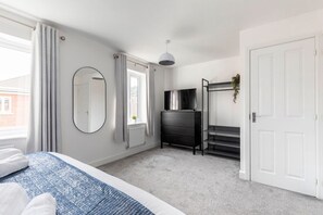 A bedroom with a bed, a dresser, a TV, a mirror, and a door.