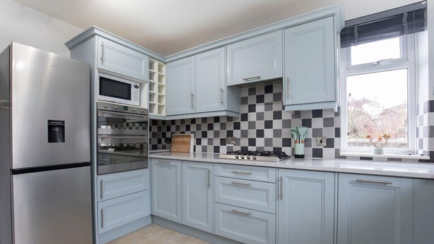 A modern kitchen with light blue cabinets, stainless steel appliances, and a checkered backsplash.