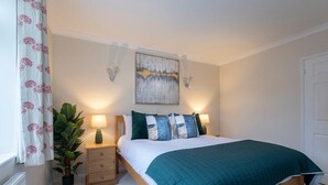 A bedroom with a bed, bedside tables, a lamp, a painting, and a potted plant.