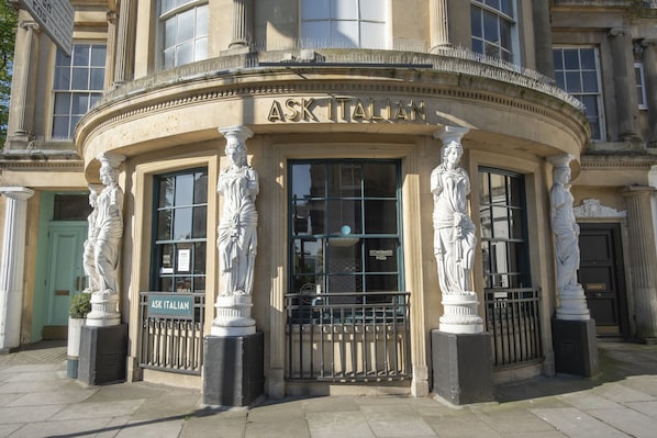 A building with classical architecture, featuring columns and statues around the entrance.