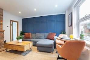 Un salon moderne avec un mur d’accent bleu, une table basse en bois, un canapé gris et un fauteuil orange.