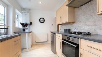 A modern kitchen with light wood cabinets, a gas stove, and a dishwasher.