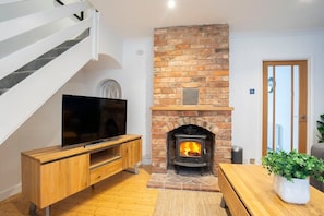 Ein Wohnzimmer mit einem Kamin aus Stein, einem Fernseher auf einem Holzboden und einer Treppe.