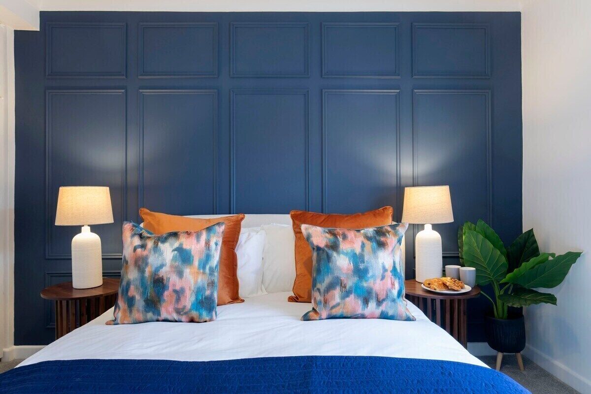 A hotel room with a large bed, two bedside lamps, a nightstand with a plate of food, and a potted plant.