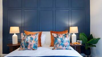 A hotel room with a large bed, two bedside lamps, a nightstand with a plate of food, and a potted plant.