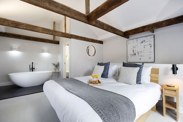 A modern bedroom with a large bed, a white bathtub, and a wooden ceiling.