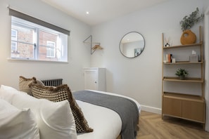 A bedroom with a bed, a radiator, a wardrobe, a mirror, and a window with a view of a brick building.