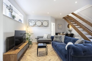 A modern living room with a blue sofa, a grey armchair, a wooden coffee table, and a TV on a wooden stand.
