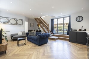 Un salon moderne avec un canapé, une table basse et un escalier menant à un balcon.