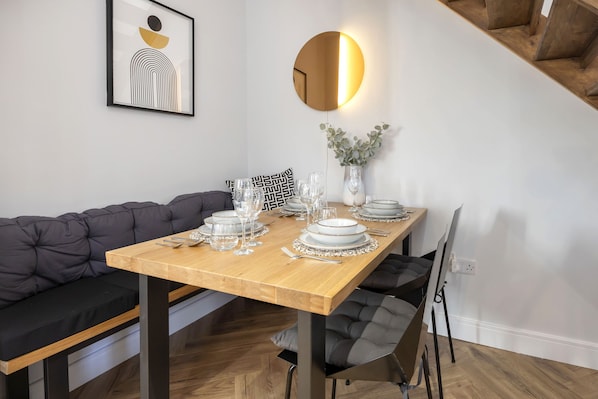 A dining area with a wooden table set for four, a grey sofa, and a round mirror with a light fixture.