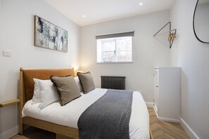 A bedroom with a bed, a radiator, a window, and a wall-mounted artwork.