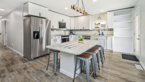 A modern kitchen with white cabinetry, stainless steel appliances, a central island with stools, and a hanging light fixture.