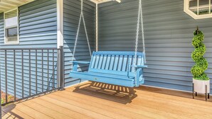 A blue porch swing with a wooden deck, a metal railing, and a potted plant.