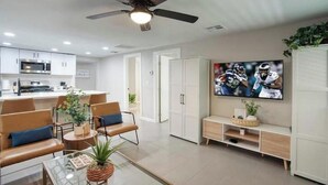 Un salon moderne doté d’un téléviseur à écran plat, d’un ventilateur de plafond et d’un coin cuisine à l’arrière-plan.