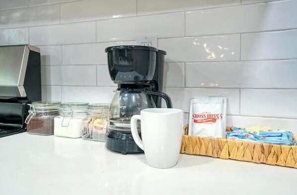 A kitchen counter with a coffee maker, a white mug, jars of sugar and spices, and a box of paper towels.