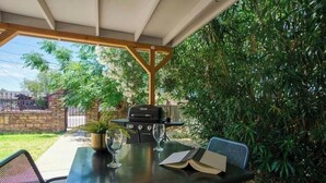 Une terrasse extérieure avec une table, des chaises, un barbecue et un livre.