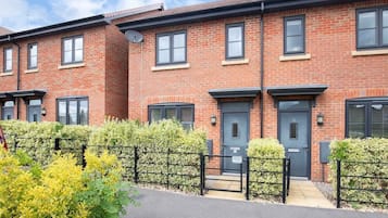 A row of red brick townhouses with black-framed windows and doors, a gated driveway, and a well-maintained hedge.