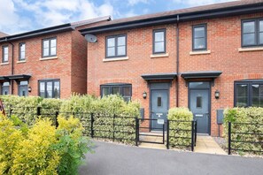 A row of red brick townhouses with black-framed windows and doors, a gated driveway, and a well-maintained hedge.