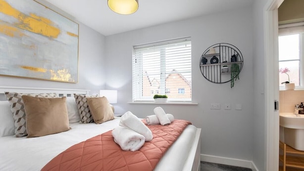 A bedroom with a bed, pillows, a window, a wall-mounted shelf, and a view of the outside.