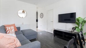 A modern living room with a grey sectional sofa, a black entertainment unit, and a flat-screen TV. - Modern Two Bedroom Two Bathroom Home (Gloucestershire)