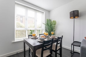 Un comedor con una mesa dispuesta para cuatro personas, una planta en maceta y una lámpara de pie.