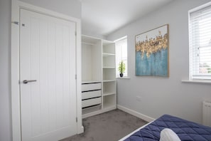 Un dormitorio con cama, armario blanco, estantería empotrada y ventana con persianas.