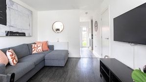 A modern living room with a grey sectional sofa, a flat-screen TV, and a large abstract painting on the wall.