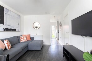 A modern living room with a grey sectional sofa, a flat-screen TV, and a large abstract painting on the wall. - Modern Two Bedroom Two Bathroom Home (Gloucestershire)