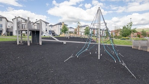 A playground with climbing structures and a slide, surrounded by residential buildings.