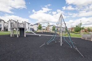 A playground with climbing structures and a slide, surrounded by residential buildings. - Modern Two Bedroom Two Bathroom Home (Gloucestershire)