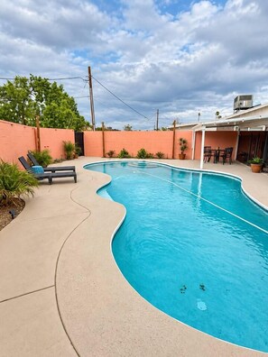 A curved swimming pool with lounge chairs and a patio area. - Tempe Pool + Hot Tub | Games, Near ASU (Tempe)