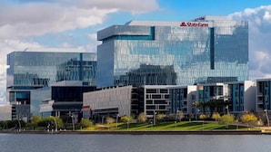 A modern building with a glass facade and a visible logo, surrounded by a landscaped area with trees and a body of water. - Tempe Getaway w/Pool & Near ASU! (Tempe)