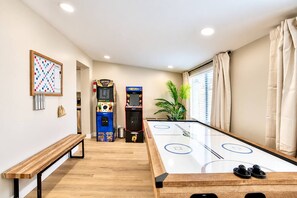 A room with a foosball table, two arcade games, a bench, and a plant. - Tempe Pool + Hot Tub | Games, Near ASU (Tempe)