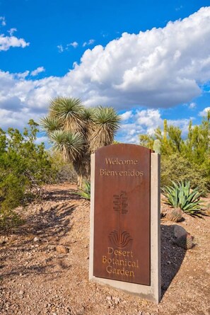 Velkomstskilt til Desert Botanical Garden med en klar himmel og ørkenvegetation i baggrunden.