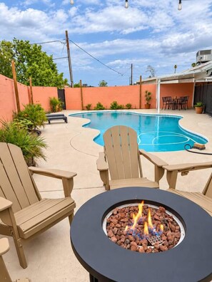 A backyard with a swimming pool, outdoor seating, and a fire pit.