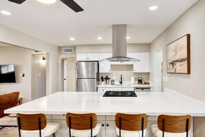 A modern kitchen with a central island, stainless steel appliances, and wooden chairs. - Tempe Pool + Hot Tub | Games, Near ASU (Tempe)