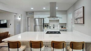 A modern kitchen with a central island, stainless steel appliances, and a flat-screen TV mounted on the wall. - Tempe Getaway w/Pool & Near ASU! (Tempe)