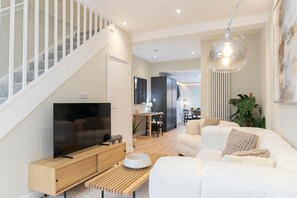A modern living room with a TV, sofa, and dining area. - Beautiful Montpellier Retreat (Gloucestershire)