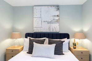 A neatly made bed with a dark headboard, two bedside tables with lamps, and a large abstract painting above the bed.