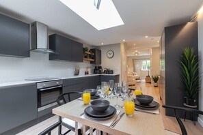 A modern kitchen with a skylight, a dining area with a table set for four, and a living space in the background.